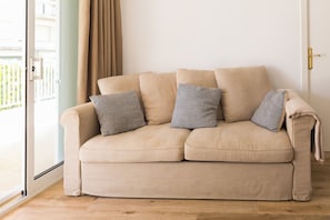 A beige sofa with patterned cushions, a glass door, and a wooden floor. - New Listing (Salou)