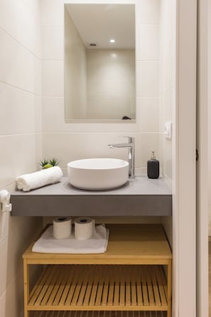 Ein modernes Badezimmer mit einem runden Waschbecken, einem Spiegel darüber und einem Holzregal darunter.
