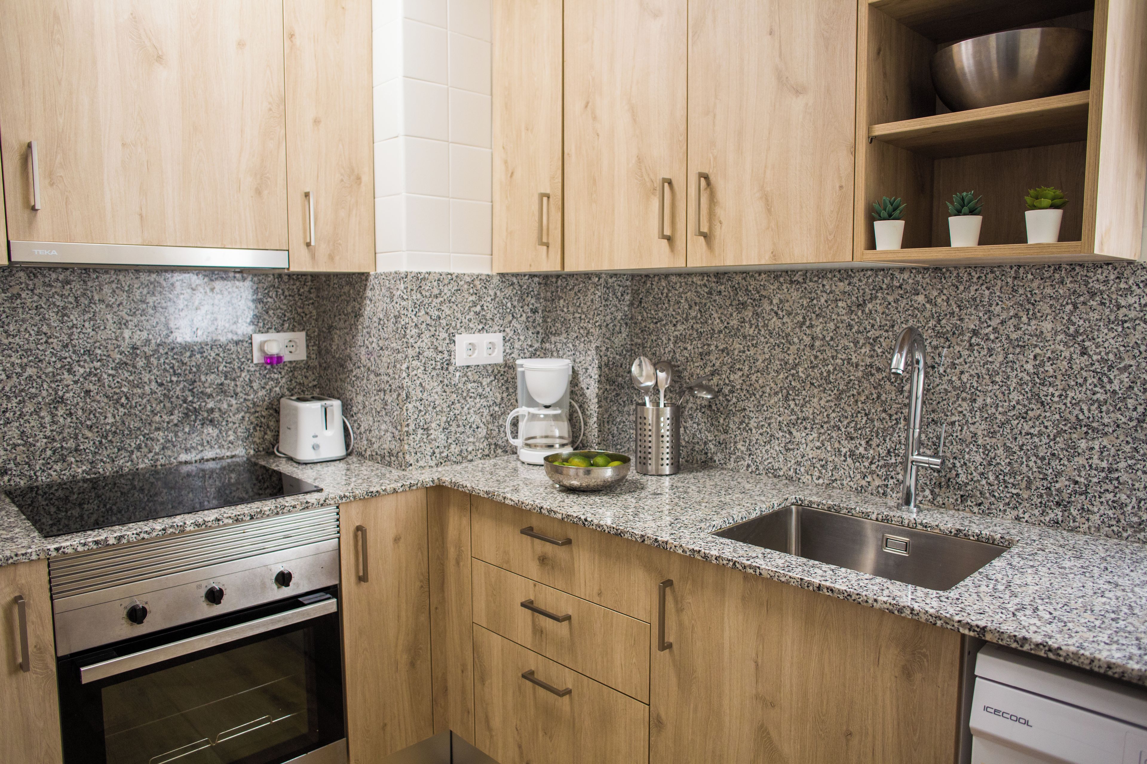 Una cocina con encimeras de granito, electrodomésticos de acero inoxidable, armarios de madera y un escurreplatos.