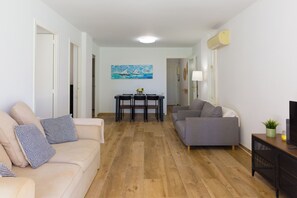 A living room with a sofa, a grey couch, a dining table with chairs, and a TV on a stand.