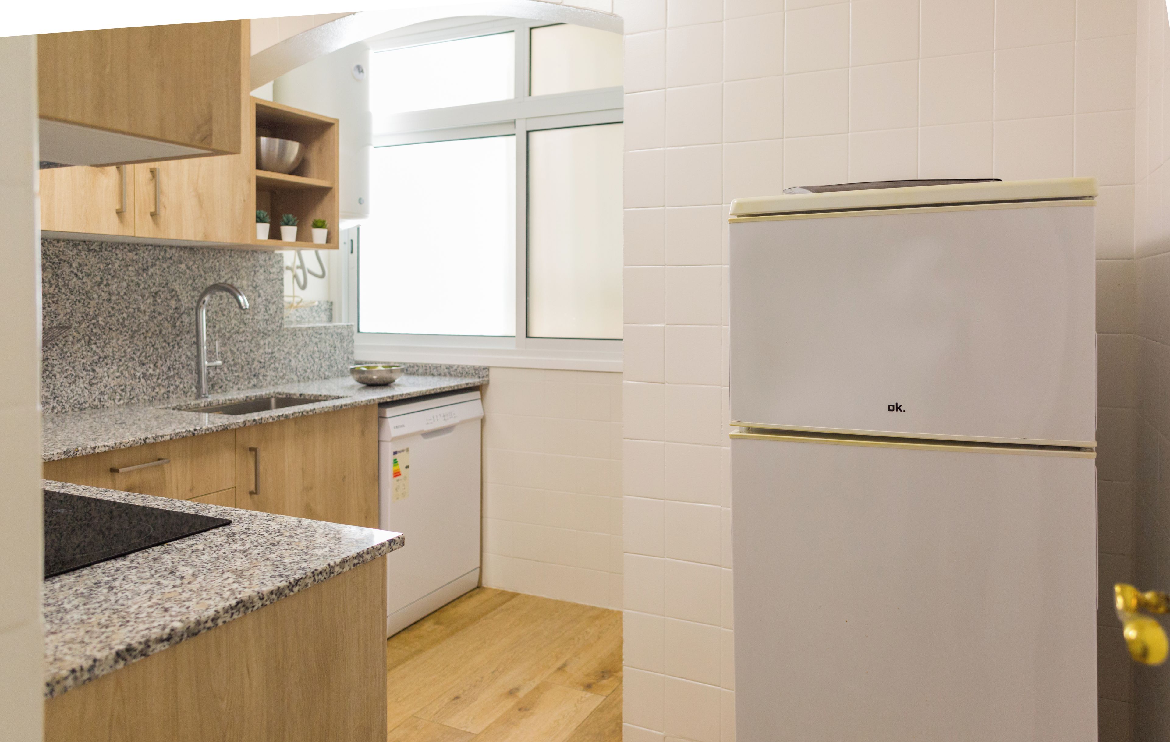 Une cuisine dotée de plans de travail en granit, d’un évier en acier inoxydable, de meubles en bois et d’un réfrigérateur blanc.