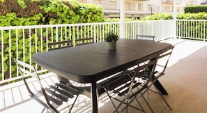 Ein schwarzer Metalltisch mit vier Stühlen, einem Blumentopf und einem weißen Geländer auf einem Balkon.
