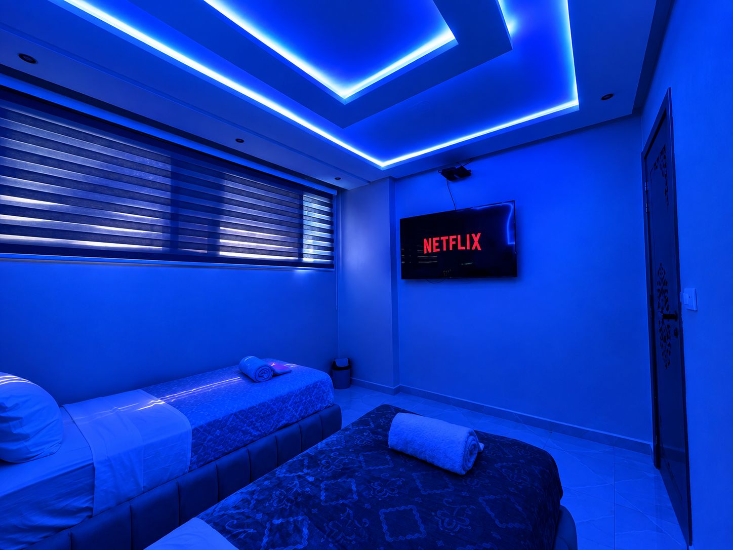 Una habitación con una cama, un sofá, un televisor montado en la pared y una ventana con persianas.