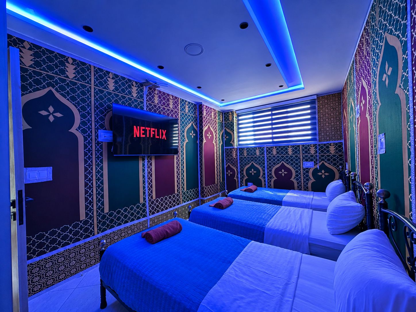 A hotel room with two beds, a TV screen displaying 'NETFLIX', and patterned walls.