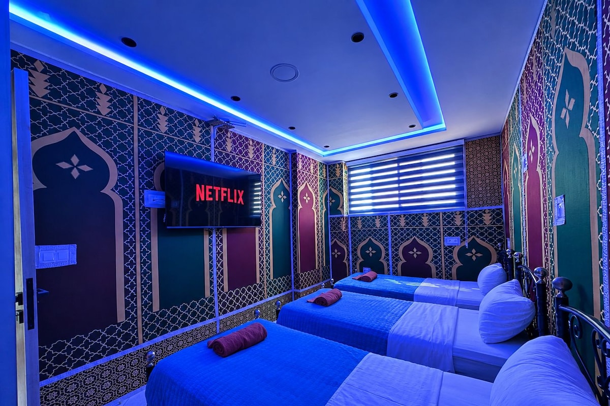 Habitació d'hotel amb dos llits, un televisor que mostra 'NETFLIX' i parets amb un disseny decoratiu.