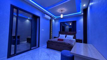 A modern bedroom with a large bed, a desk, and a sliding glass door leading to a balcony.