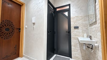 A bathroom with a black door, a wooden door with a decorative panel, a white sink with a stone backsplash, and a mirror above the sink.