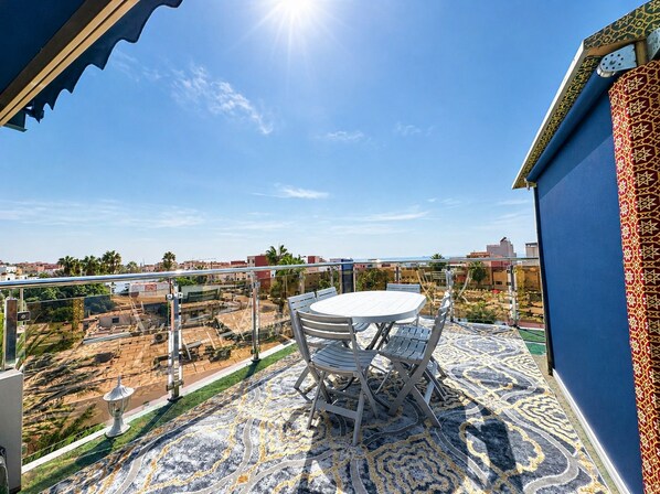 Un balcón con mesa y sillas, con vistas a una zona residencial con palmeras y edificios.
