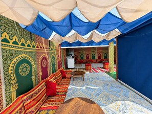 A room with patterned walls, a sofa, a table, and a view of a kitchen area.