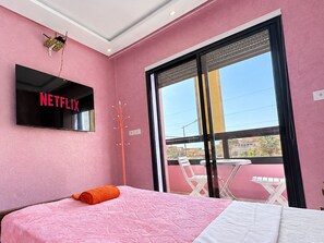A room with a bed, a TV mounted on the wall, and a balcony with chairs.