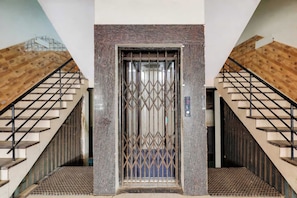 A modern elevator with a metal gate, flanked by wooden staircases with metal railings. - Hotel O Riyansh Palace (Indore)
