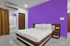 A hotel room with a bed, a nightstand, a wooden door, a bathroom with a mirror, and an air conditioning unit. - Collection O Jineshwari Hotel (Indore)