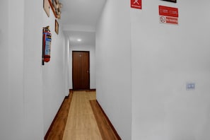 Un couloir avec un plancher en bois, un extincteur fixé au mur et une porte au fond.