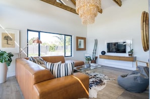 Ein modernes Wohnzimmer mit einem Ledersofa, einem Glastisch und einem großen Fernseher auf einer Holzkommode.