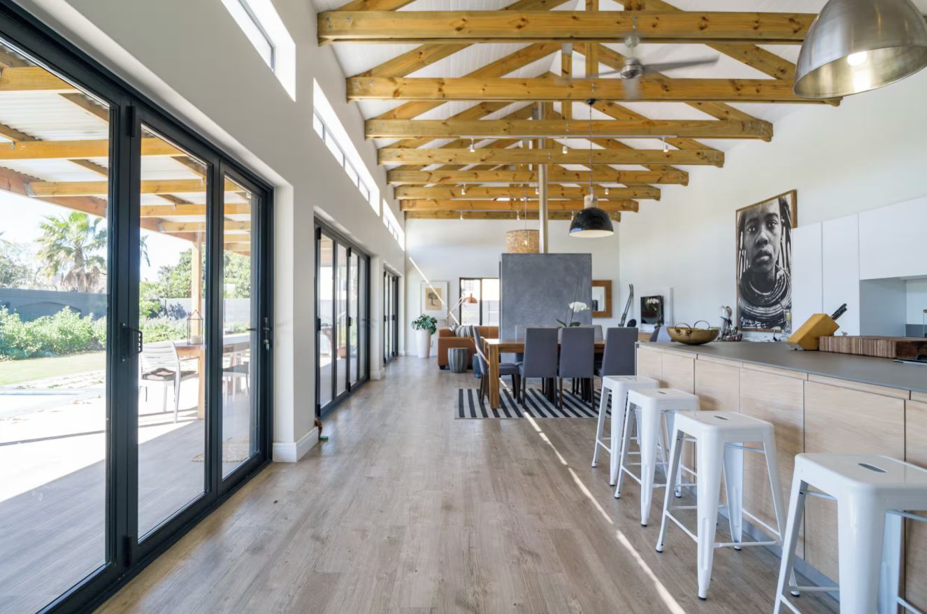 A spacious kitchen with wooden beams, a dining area with bar stools, and large windows.