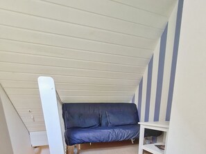 Ein Zimmer mit schrägen Wänden, einem dunkelblauen Sofa und einer weißen Regalwand.