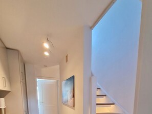 Ein Flur mit einer Treppe, die zu einer oberen Ebene führt, einer Tür am Ende und einem gerahmten Bild an der Wand.