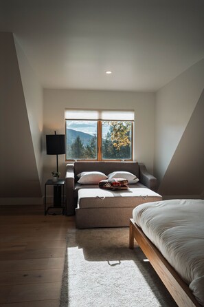 Une chambre avec un lit, un canapé, une fenêtre donnant sur des arbres et une lampe.