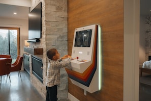 A child interacting with a wall-mounted gaming console in a modern interior with stone and wood accents. - Peak Foliage - 7BR Windham Mountain Estate (Windham)