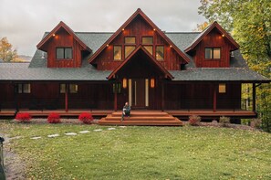 Une grande maison en bois à plusieurs étages, dotée d’un porche avant imposant et d’un jardin aménagé.