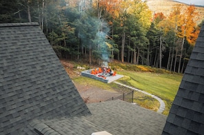 A rooftop patio with a fire pit and outdoor seating, surrounded by a forested area. - Peak Foliage - 7BR Windham Mountain Estate (Windham)