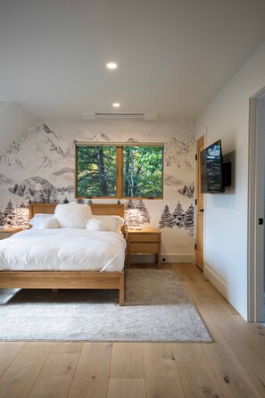 A bedroom with a bed, nightstands, a TV, and a window with a view of trees. - Peak Foliage - 7BR Windham Mountain Estate (Windham)