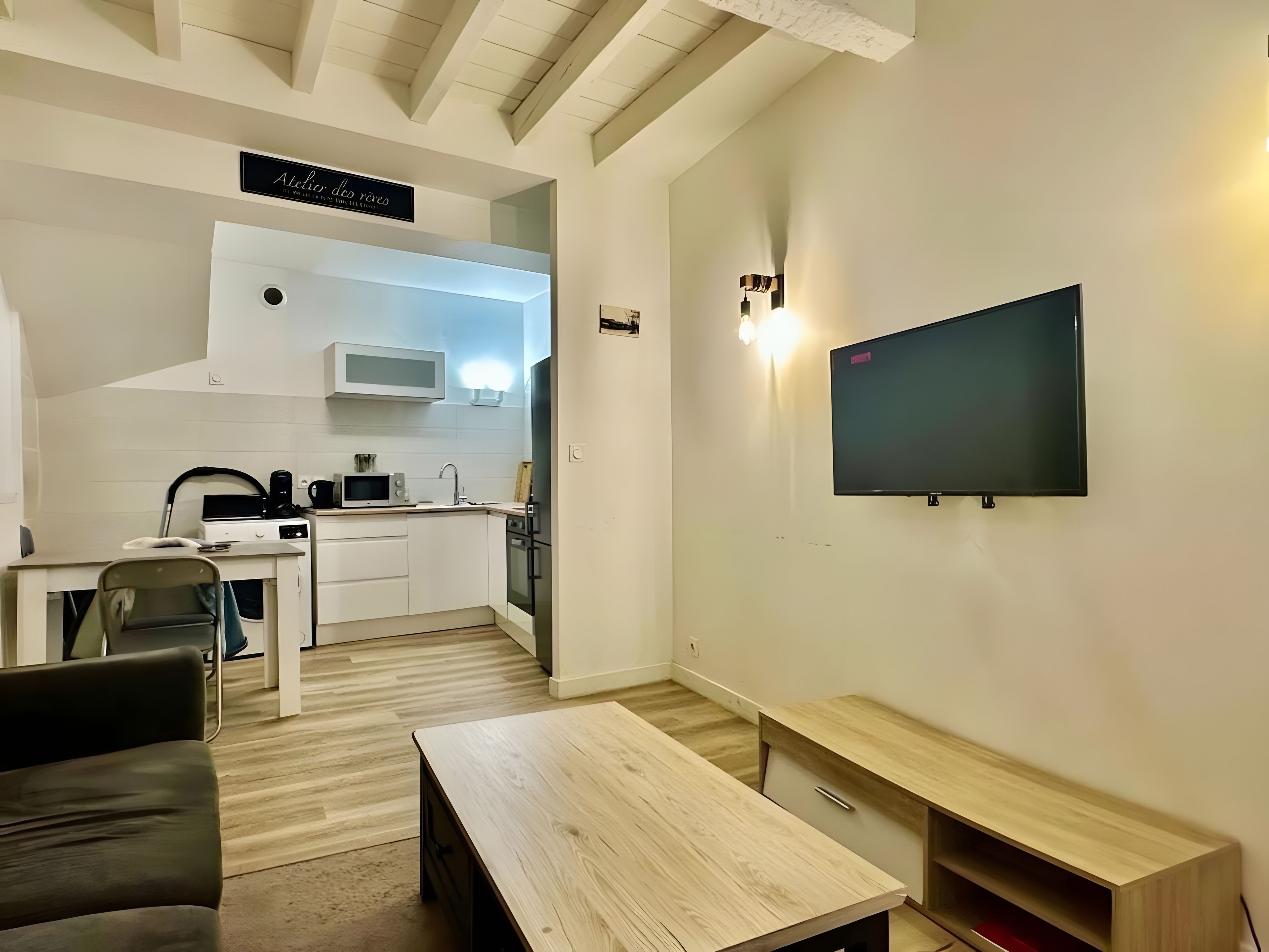 A compact living space with a kitchenette, a flat-screen TV mounted on the wall, a wooden coffee table, and a sofa.