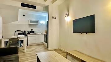 A compact living space with a kitchenette, a flat-screen TV mounted on the wall, a wooden coffee table, and a sofa.