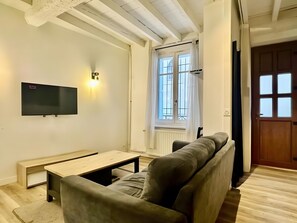 A living room with a sofa, a coffee table, a flat-screen TV mounted on the wall, and a window with curtains. - Holiday Home 'Maison Jebari' (Carcassonne)