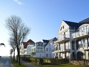 A row of modern, multi-story residential buildings with balconies, a clear sky, and a pathway lined with trees. - Rothtraut Remise 4 (Wyk auf Foehr)