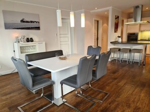 A modern dining area with a white table, grey chairs, and pendant lighting. - Rothtraut Remise 4 (Wyk auf Foehr)