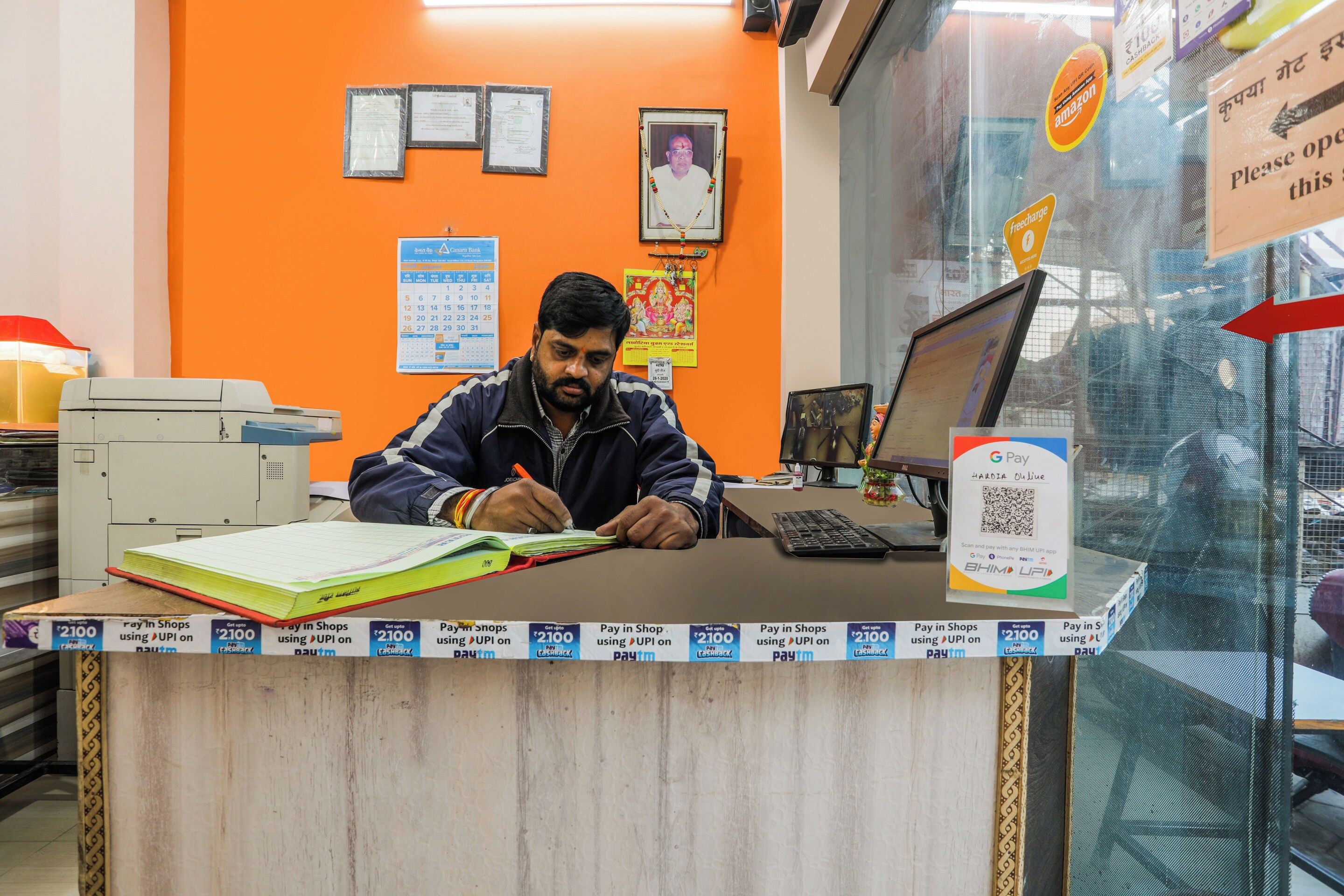 A man at a counter with a computer and documents, surrounded by various payment options and a calendar.