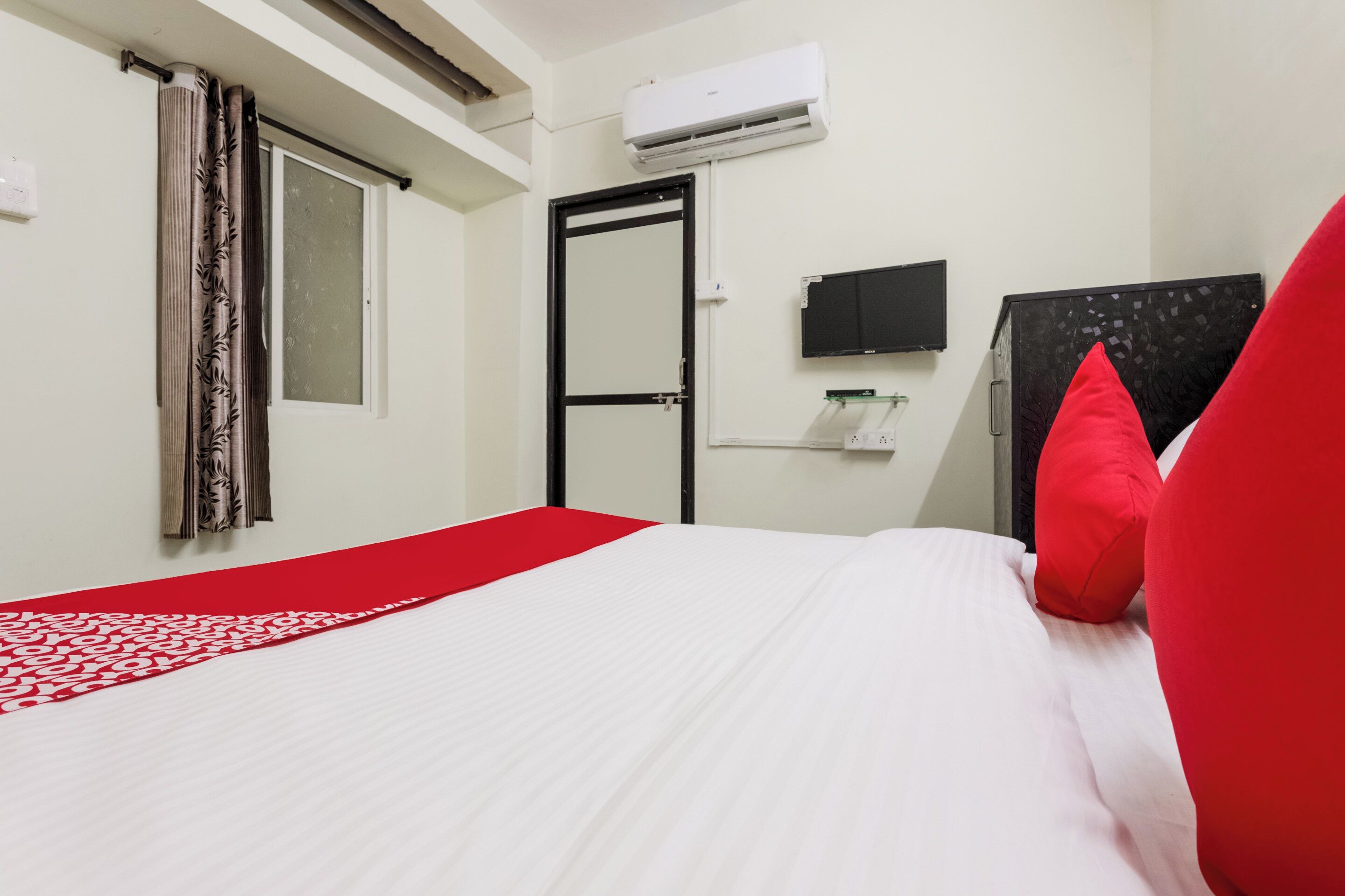 A hotel room with a bed, a window with curtains, an air conditioning unit, a flat-screen TV, and a wardrobe.