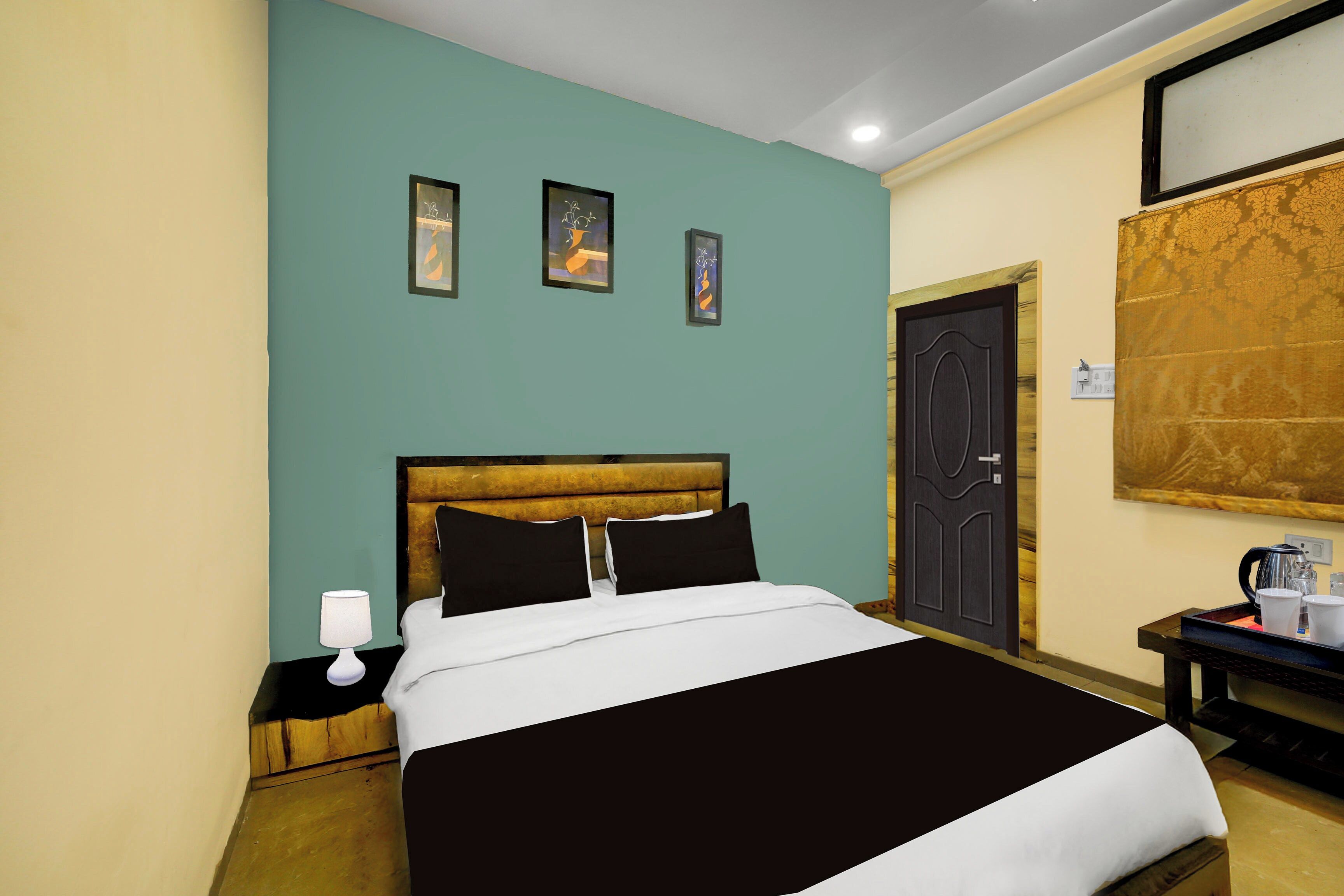 Una habitación de hotel con cama, mesita de noche, lámpara, cafetera y puerta.