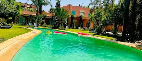 A swimming pool with clear water, surrounded by palm trees and a building with a red roof.