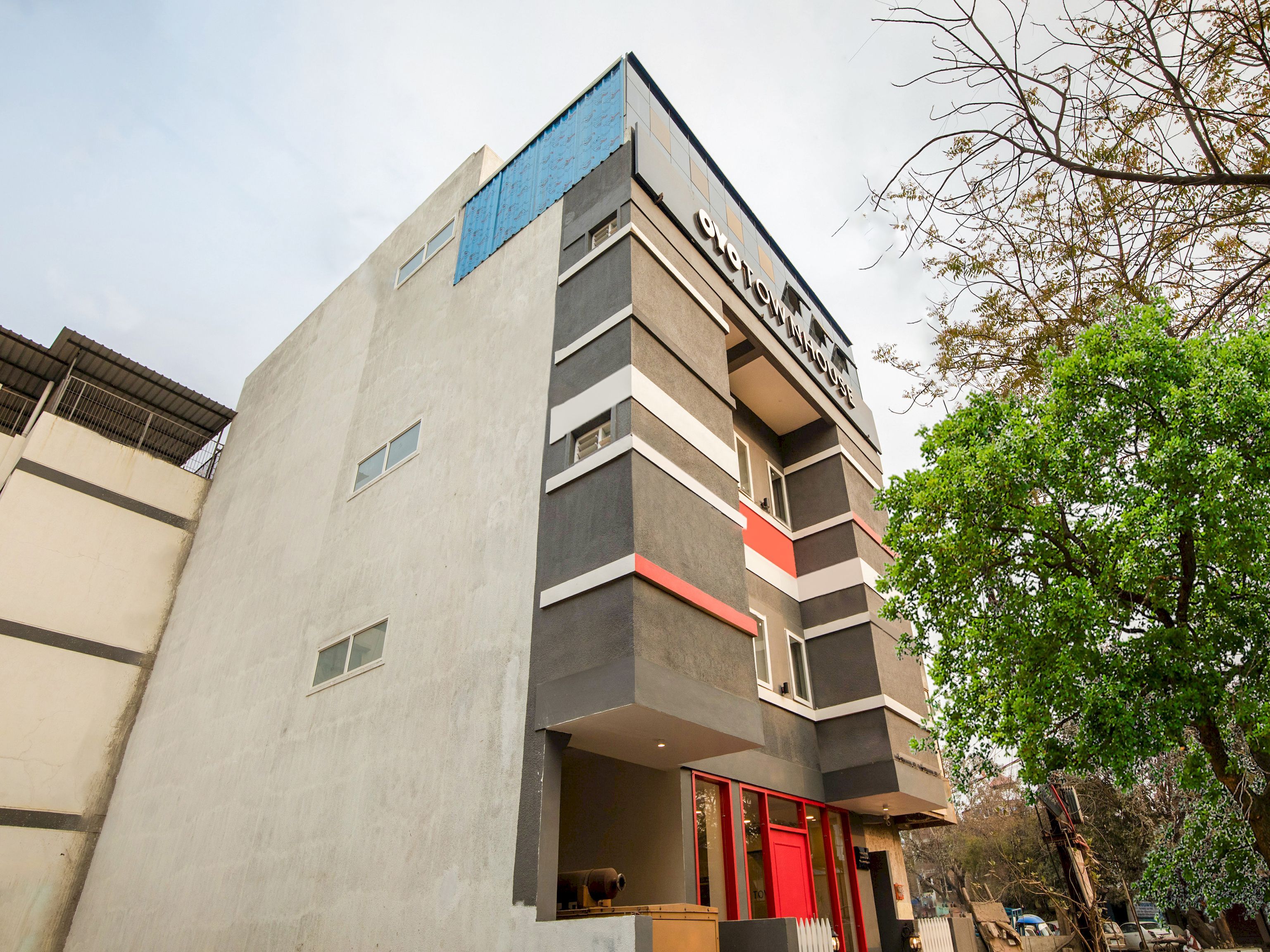 Un edificio de varios pisos con un diseño arquitectónico moderno, que presenta una entrada destacada con una puerta roja y un letrero encima.