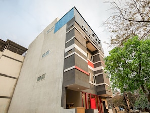 Un edificio de varios pisos con un diseño arquitectónico moderno, que presenta una entrada destacada con una puerta roja y un letrero encima.