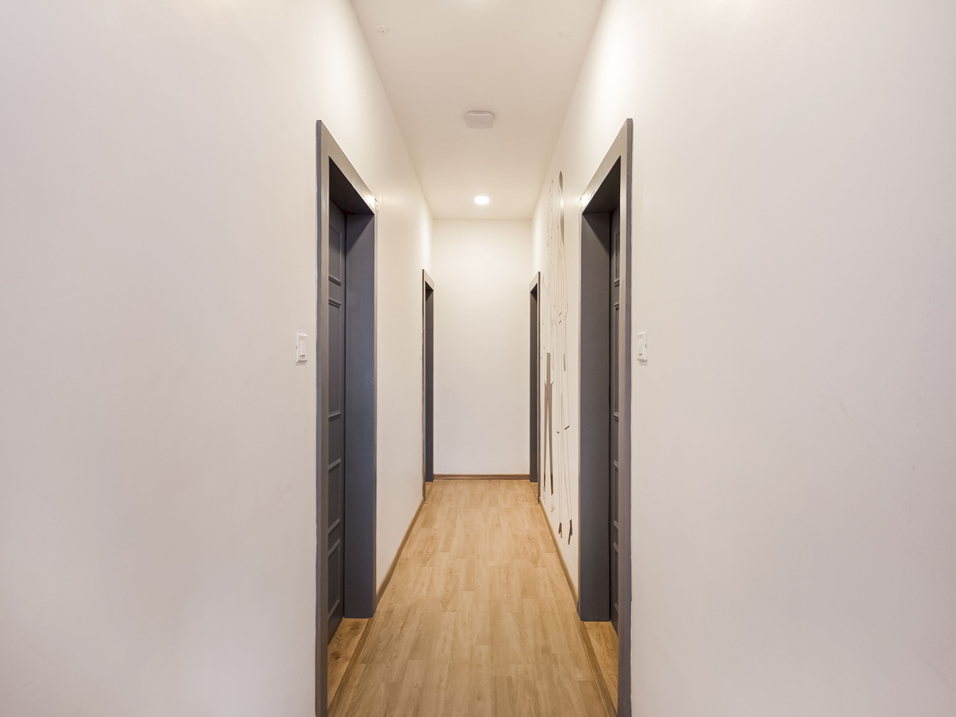 Um corredor estreito com piso de madeira e paredes brancas, que dá para uma porta no final.