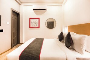 Una habitación de hotel con una cama, un cuadro enmarcado, un espejo redondo y un equipo de aire acondicionado.