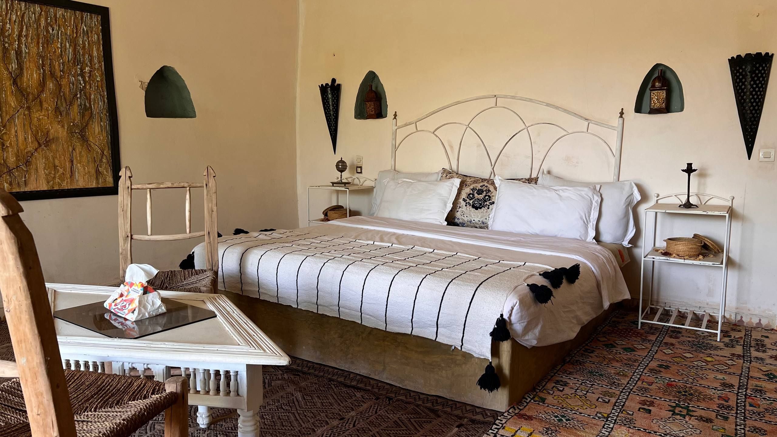 Un dormitorio ordenado con cama, mesitas de noche, una silla y un cuadro en la pared.