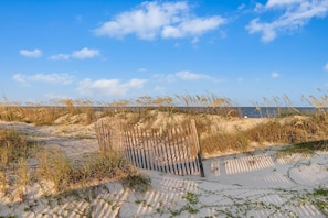 Een zandstrand met duinen en een houten hek.