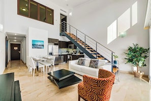 A modern living room with a staircase, dining area, and kitchen. - Loft-Style 2BR Condo w/ Pool View, Palm Beach (Noord)