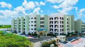 A multi-story hotel with a central courtyard, balconies, and a parking area. - Loft-Style 2BR Condo w/ Pool View, Palm Beach (Noord)