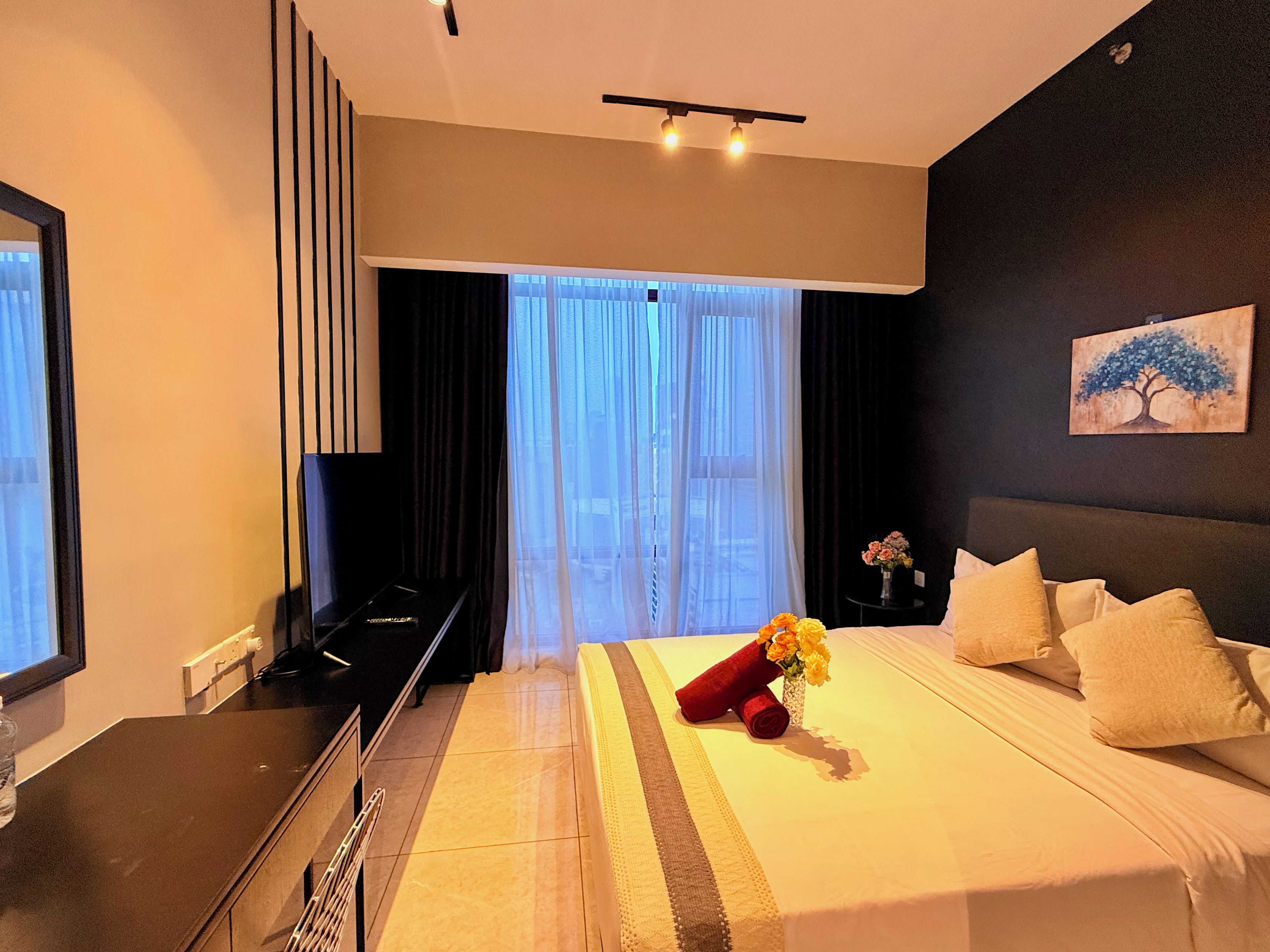 Habitación de hotel con cama, televisión, escritorio y ventana con cortinas.