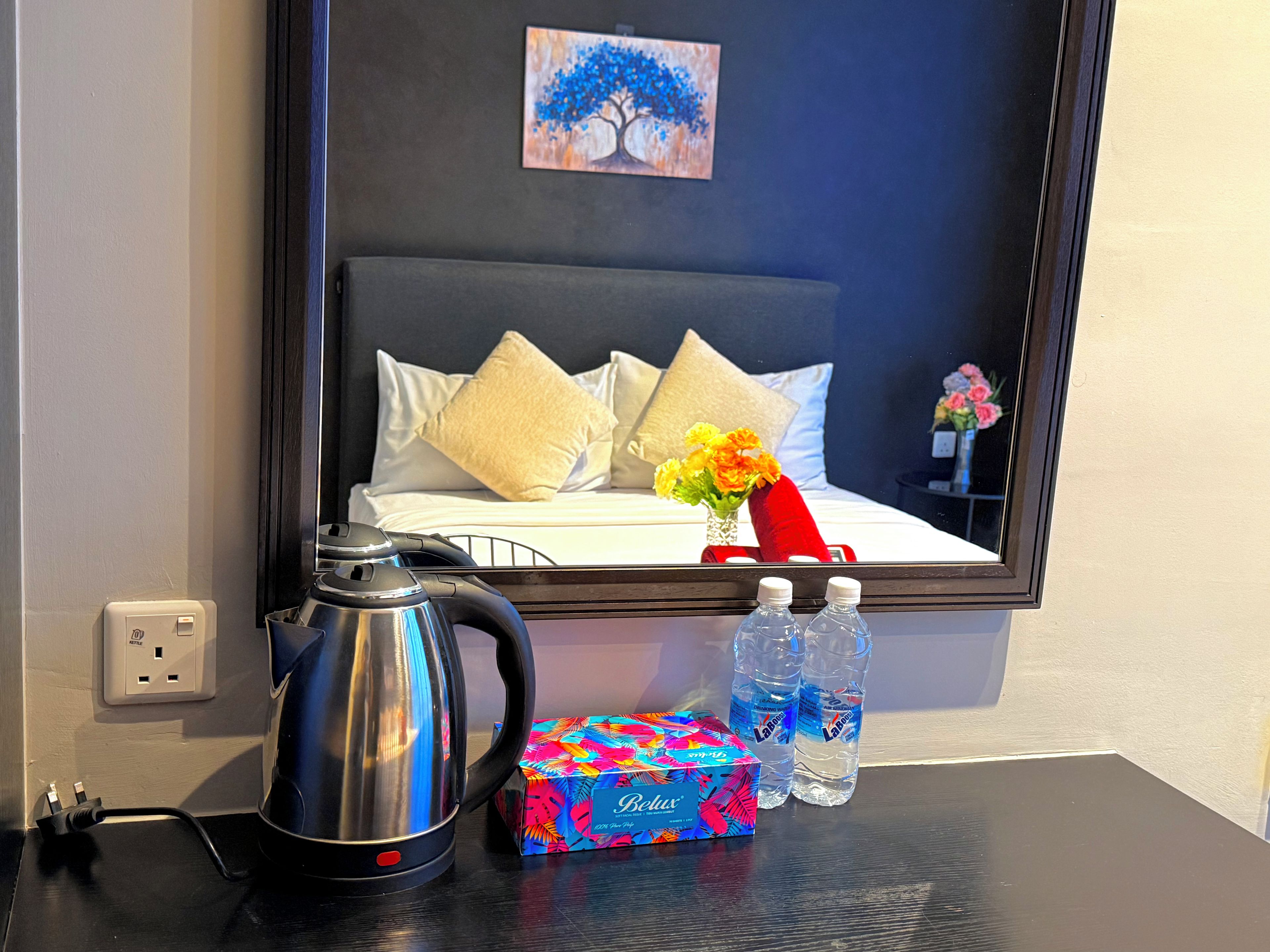 Habitación de hotel con cama, un cuadro, hervidor de agua, caja de pañuelos y botellas de agua.
