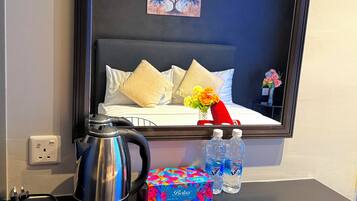 Habitación de hotel con cama, un cuadro, hervidor de agua, caja de pañuelos y botellas de agua.