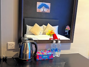 Habitación de hotel con cama, un cuadro, hervidor de agua, caja de pañuelos y botellas de agua.