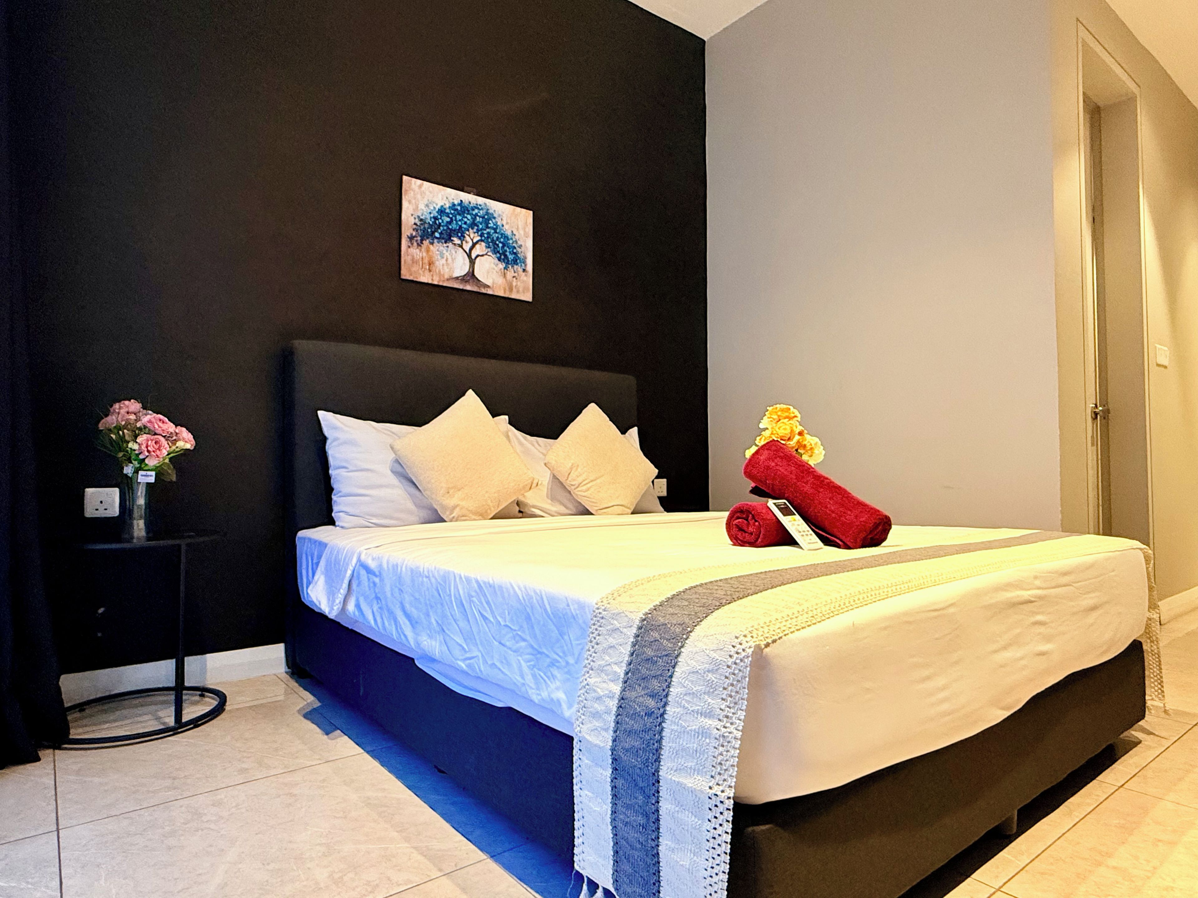 A hotel room with a bed, a nightstand, a vase with flowers, and a painting on the wall.