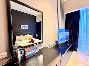 A hotel room with a bed, a TV on a stand, a kettle, a water bottle, and a small table with a box. - Axon Residence KL Pavilion  (Kuala Lumpur)