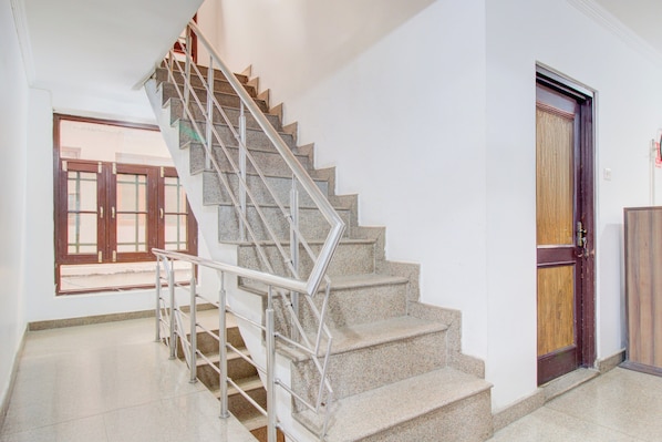Una escalera con barandillas metálicas que conduce a un rellano, una puerta de madera y una ventana con vistas al exterior.